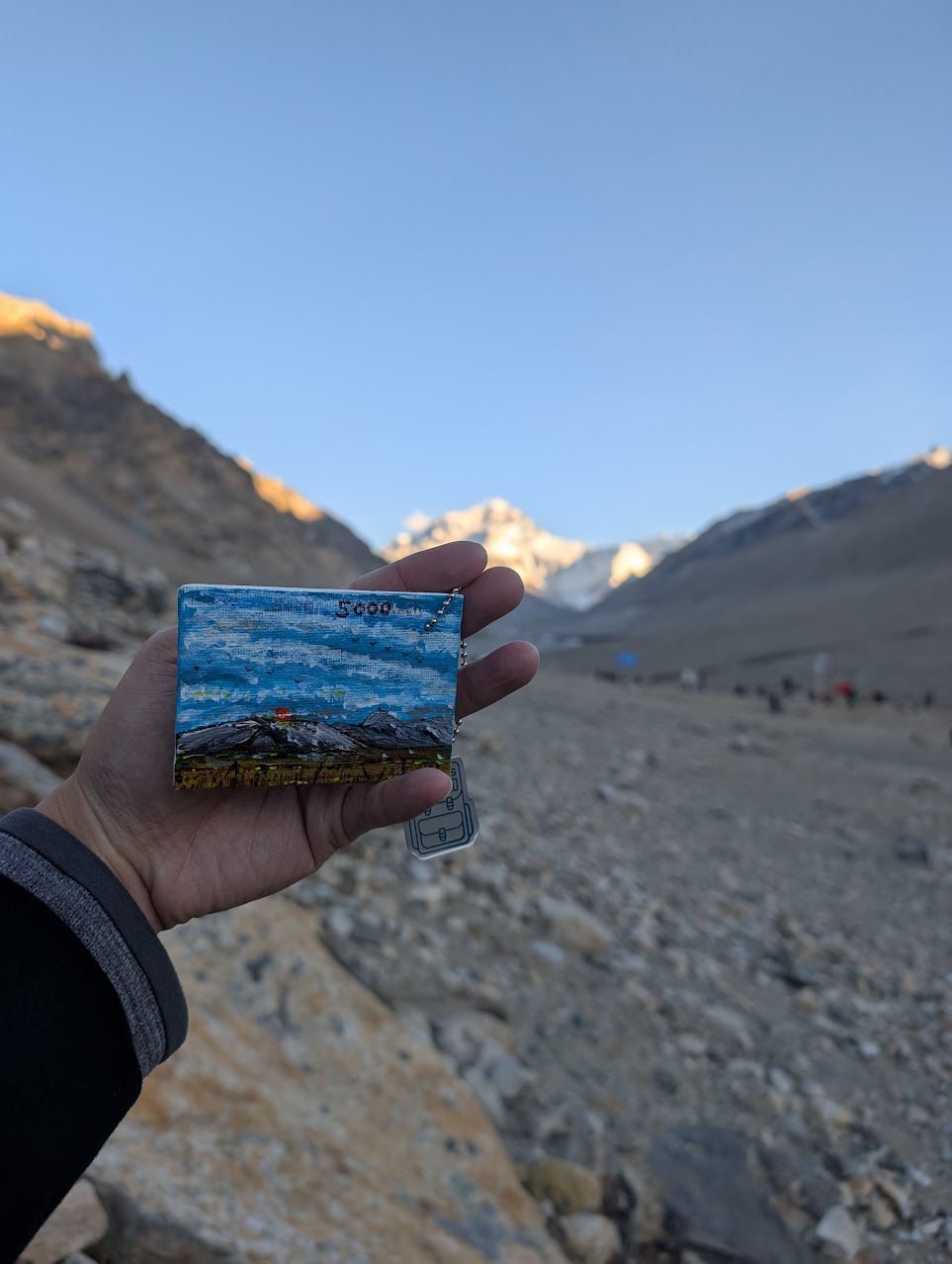 A small painting held up with Mount Everest in the background